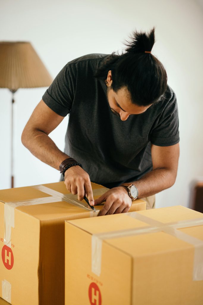 Man with dark hair in ponytail sealing a cardboard box - Visit rsd-storage.com. 